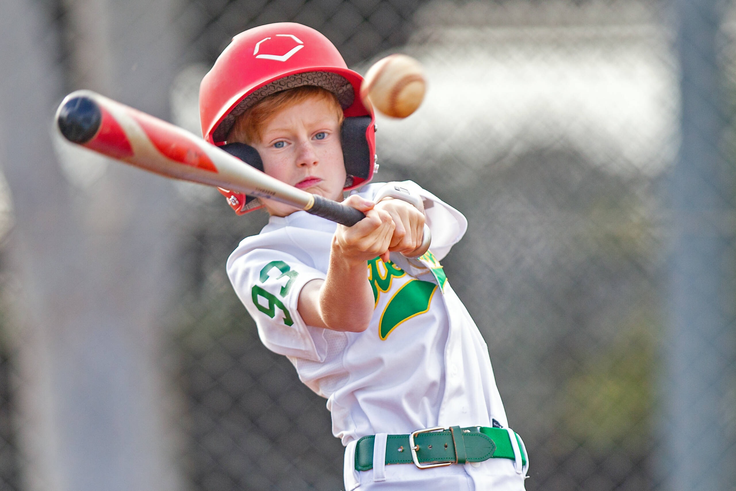 boy swinging bat just about to make contact with a pitched baseball